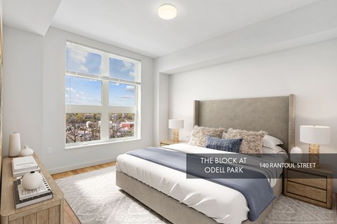 A bedroom with a large bed, a window with a view of a cityscape, and a nightstand with a lamp.