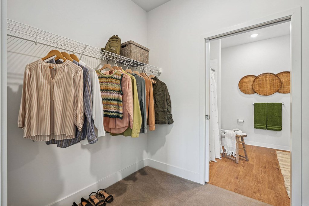 a closet with clothes hanging on a rack and a door to a bathroom