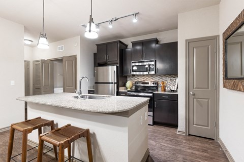 a kitchen with black cabinets and a white counter top with two stools in front of it