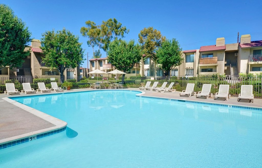 a large swimming pool with lounge chairs and buildings in the background
