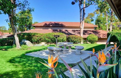 a patio with a stone table and benches in a garden