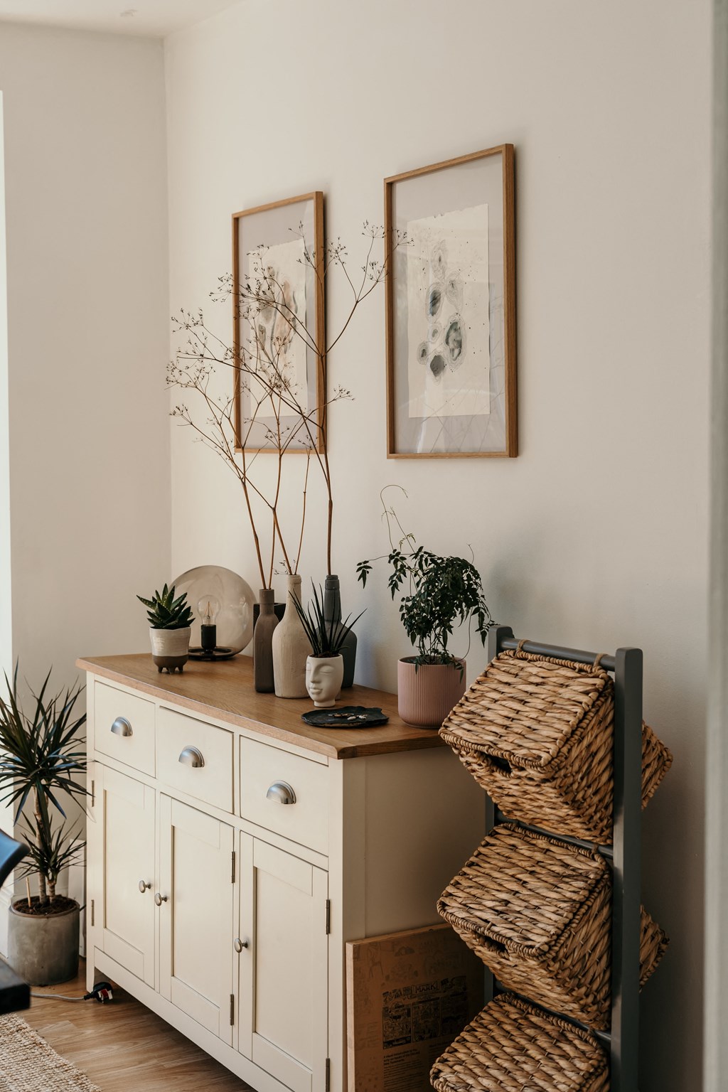 a corner of a room with a white cabinet and a shelf with baskets and plants