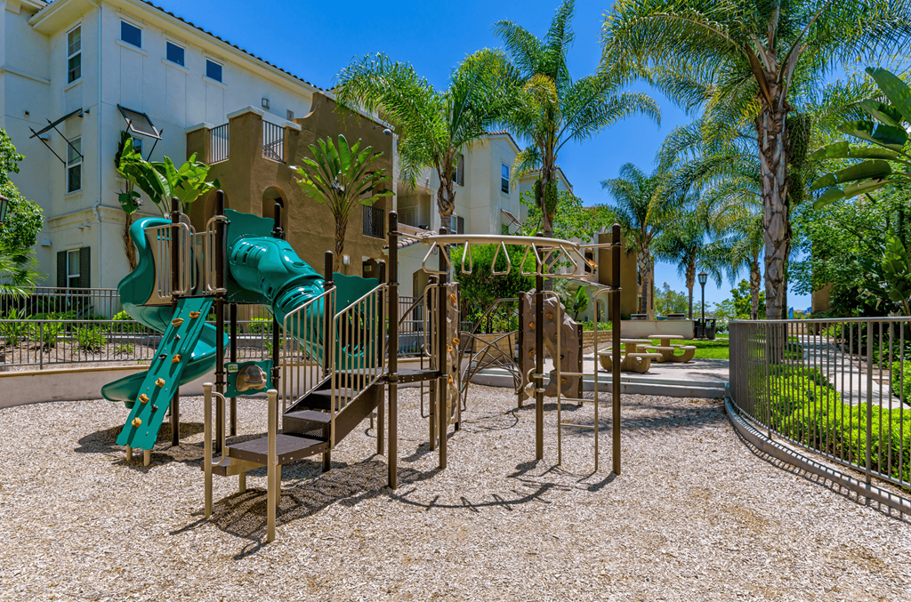 A playground with a green slide and a brown swing set.