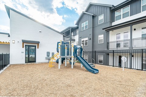 A playground with a yellow slide and a green slide in front of a white building.