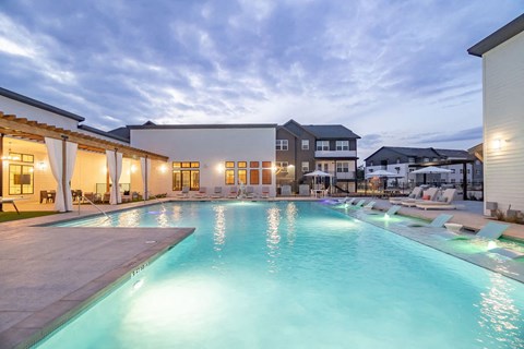 A large outdoor swimming pool with a lit poolside area.