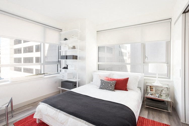 Luxury Apartments in San Francisco, CA - Trinity Place at 33 8th - Bedroom with Two Windows, Bed, Shelving, Nightstands, Carpet, Silver Chair, and Plank-Style Floor