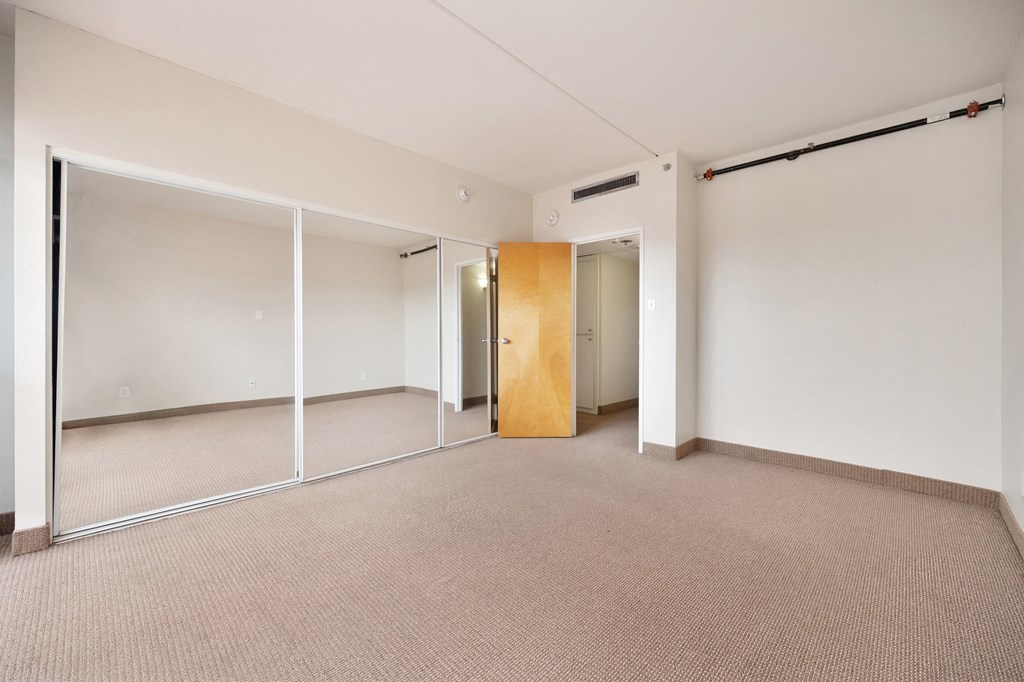 an empty room with mirrored doors and a door to a closet