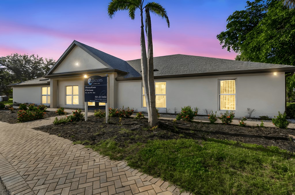 A building with a signboard in front of it is surrounded by a well-maintained garden.