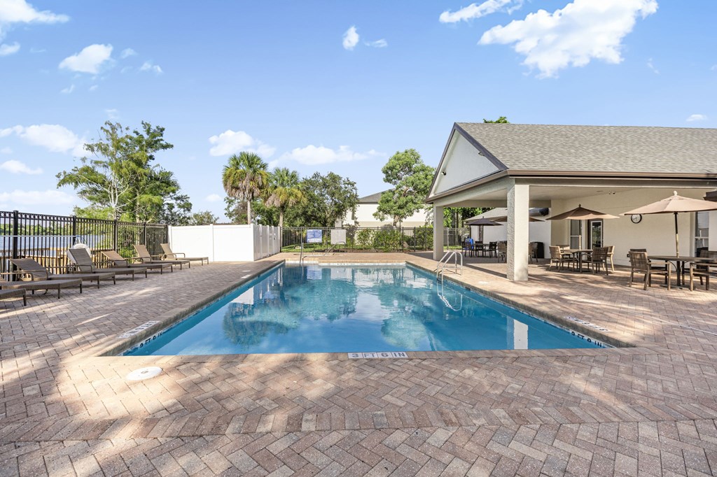 A pool surrounded by a brick patio and a house in the background.