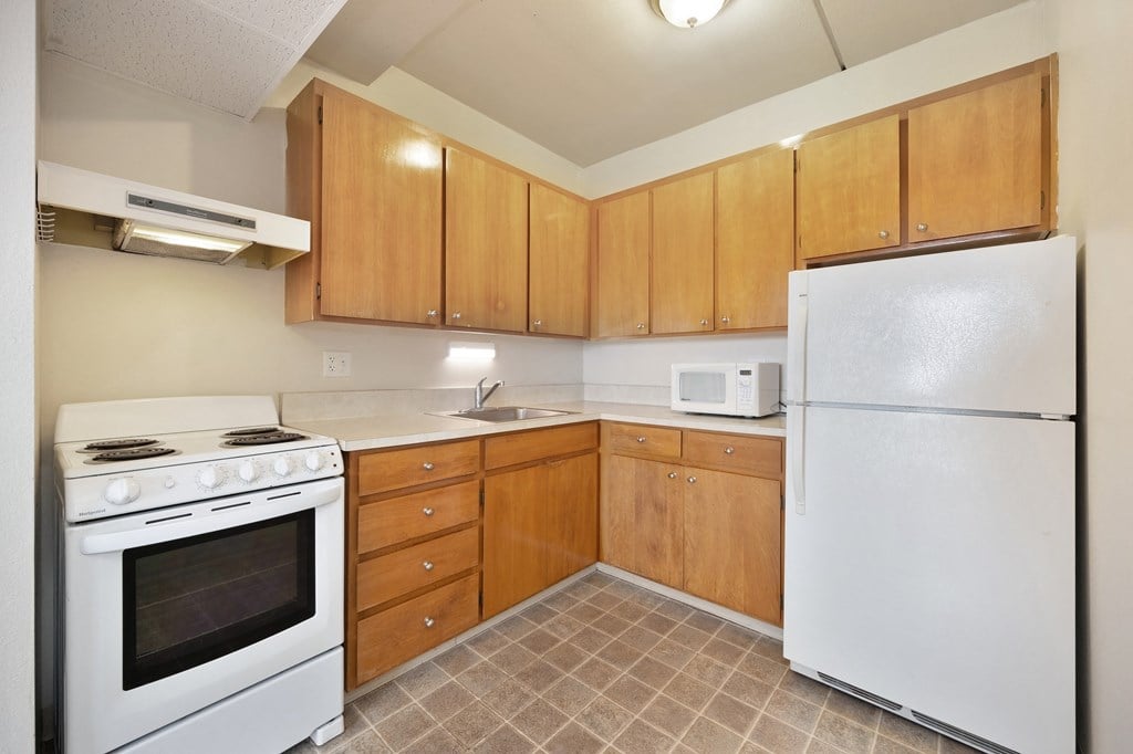 an empty kitchen with white appliances and wooden cabinets