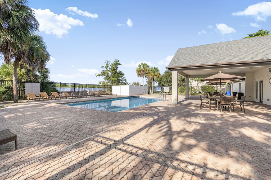 A patio with a table and chairs is surrounded by a pool.