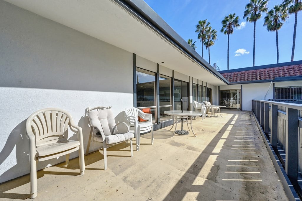 a patio with chairs and tables and a building with palm trees