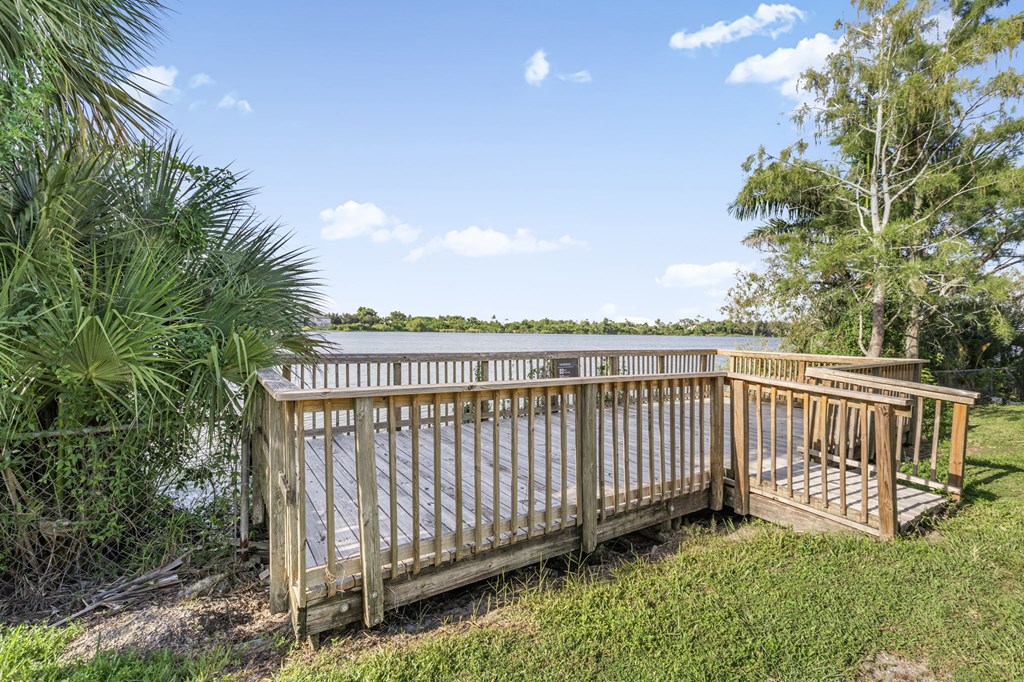 A wooden deck overlooks a body of water with trees in the background.