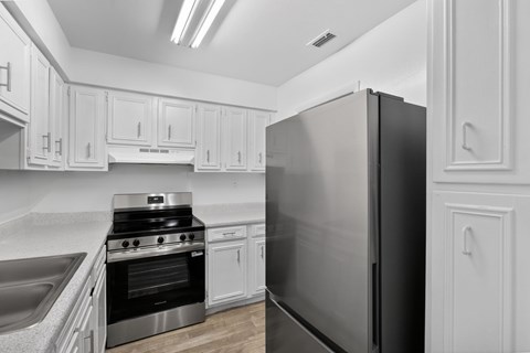 A black refrigerator stands in a kitchen with white cabinets.