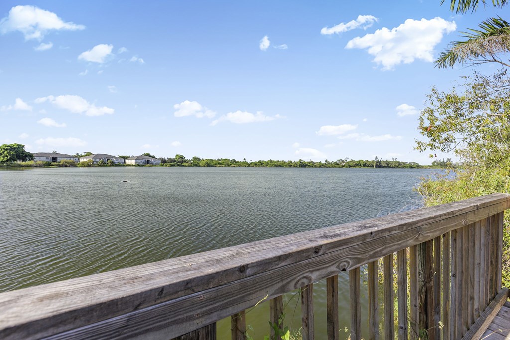 A wooden deck overlooks a body of water with a clear blue sky and some clouds.