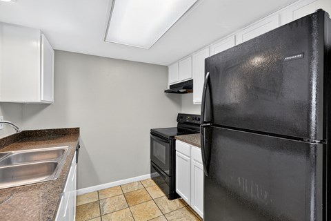 A black refrigerator is in a kitchen with white cabinets.