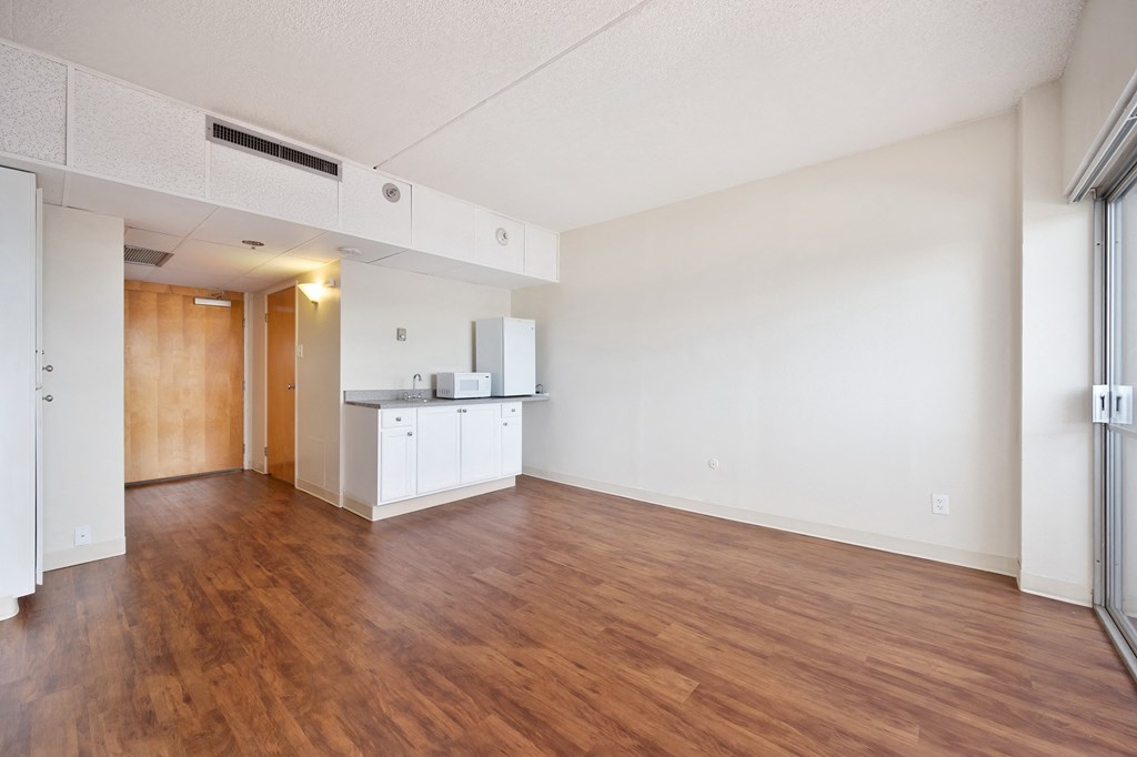 an empty living room and kitchen with wood flooring and white walls