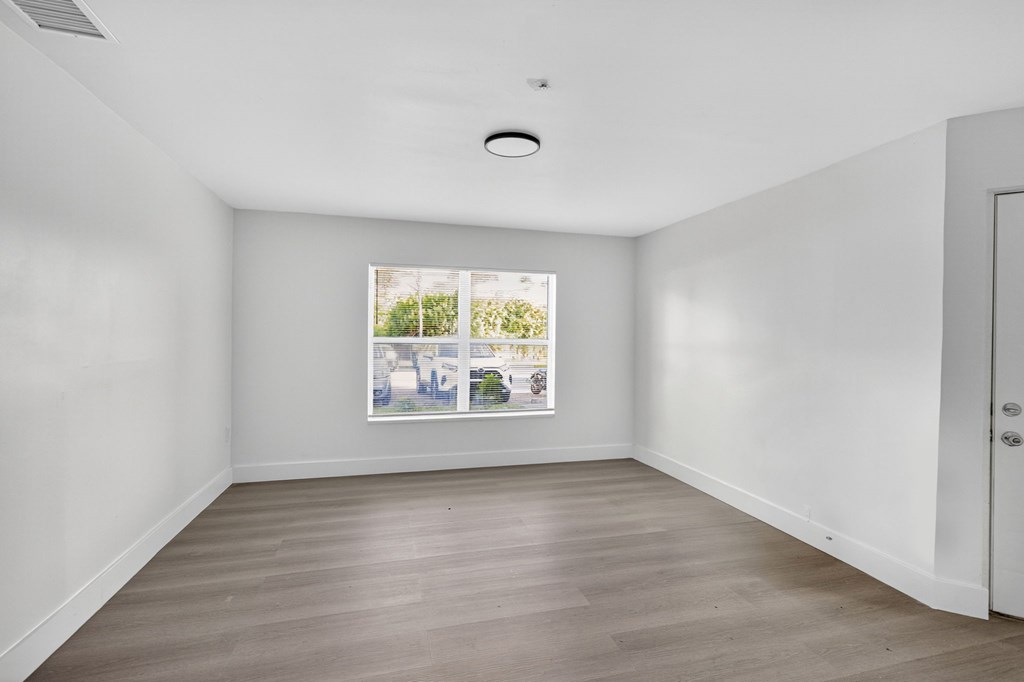 A white room with a window and a wooden floor.
