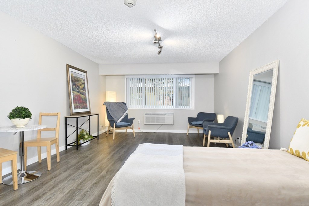 A well-lit bedroom with a bed, chair, and a dining table.