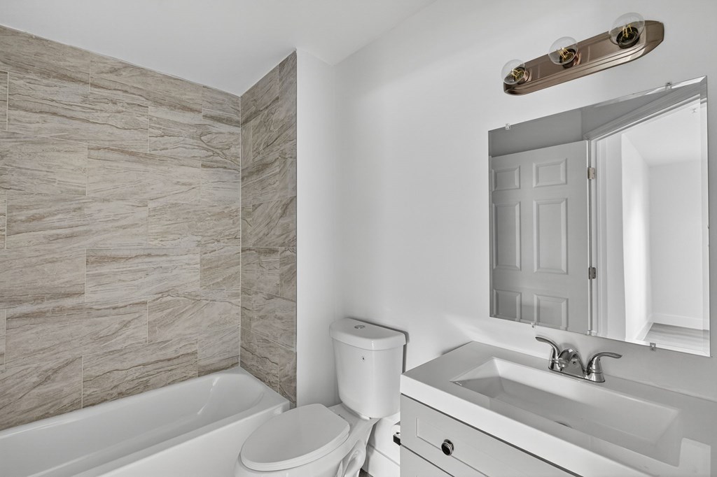 A bathroom with a white toilet, sink, and a tiled wall.