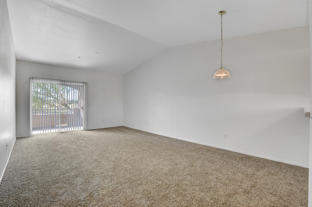 an empty living room with a sliding glass door to a balcony