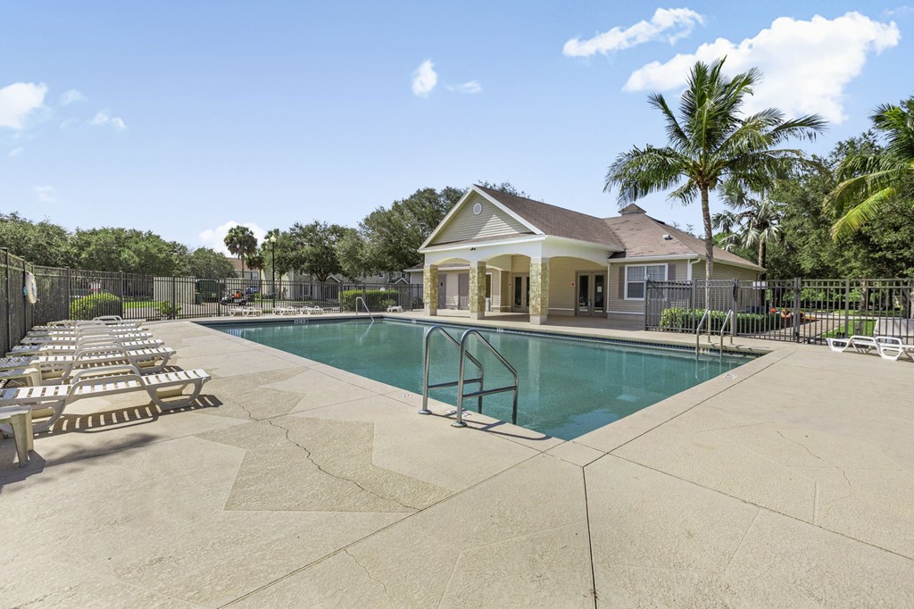 A pool area with sun loungers and a house in the background.