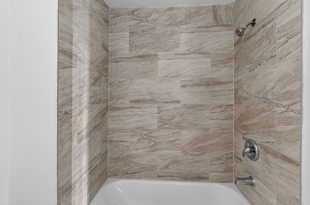 A bathroom with a tiled shower and a white bathtub.