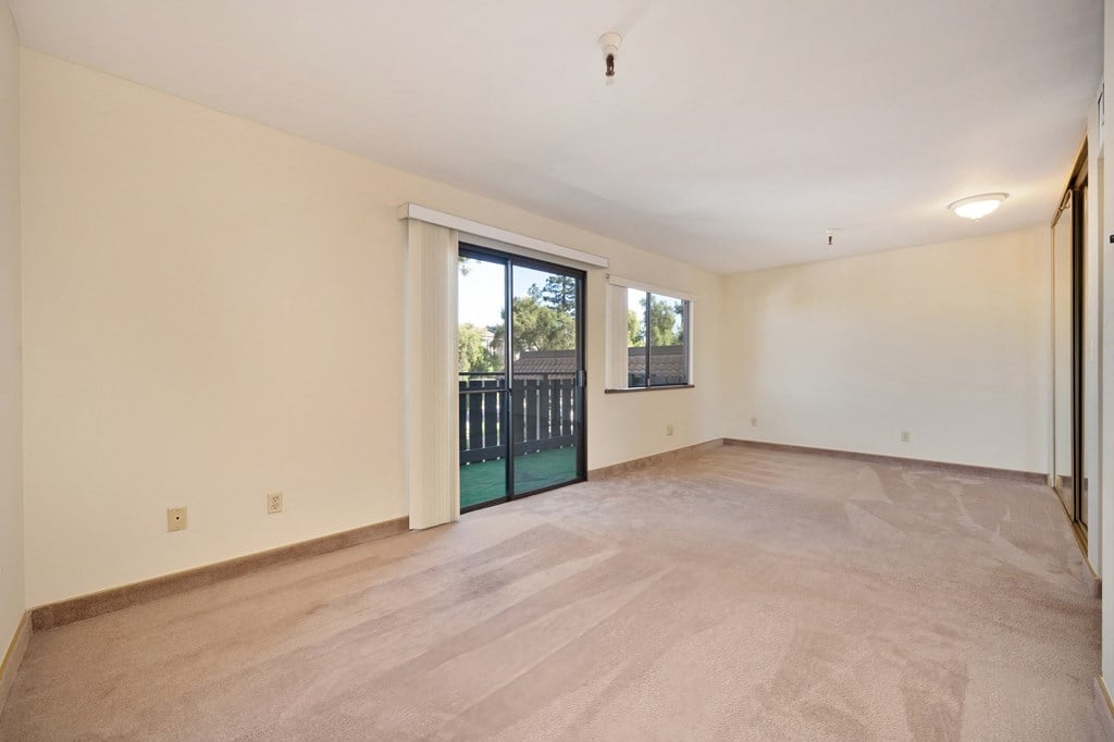 an empty living room with a sliding glass door to a balcony