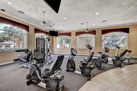 A gym with a row of exercise bikes and a television mounted on the wall.