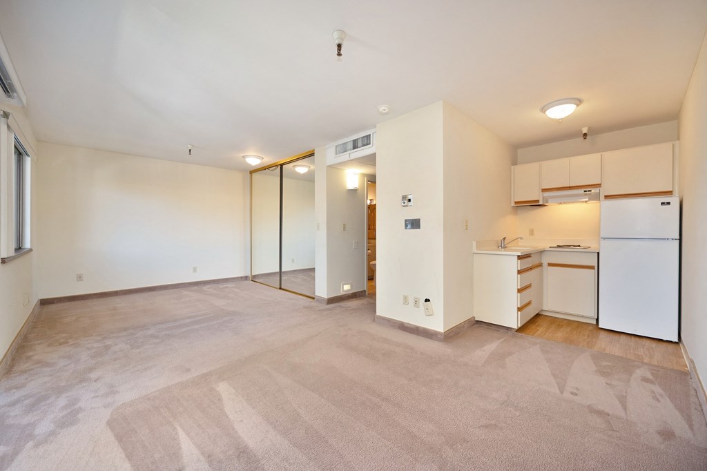 the living room and kitchen of an apartment with white cabinets and a white refrigerator
