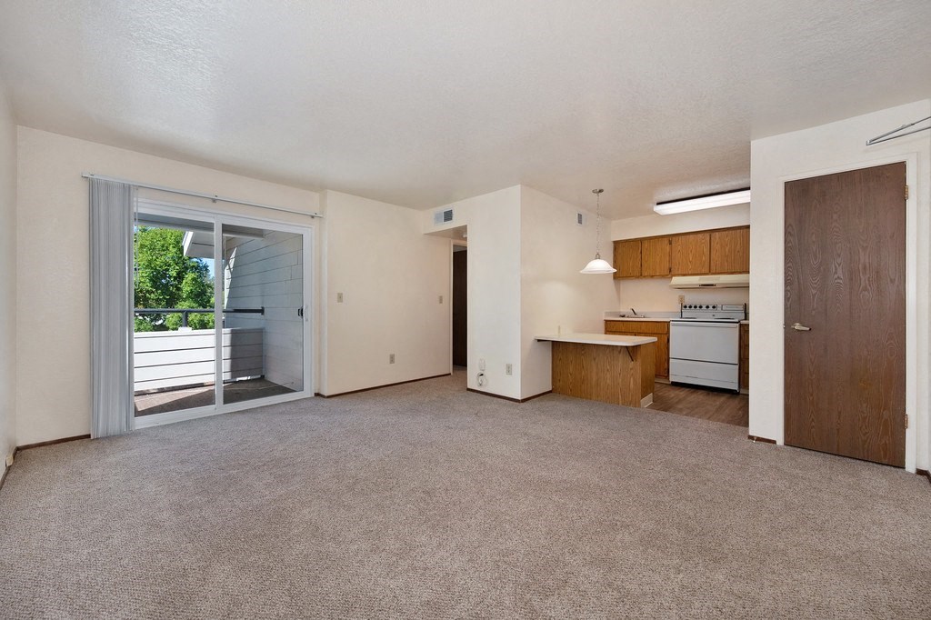 an empty living room with a kitchen in the background