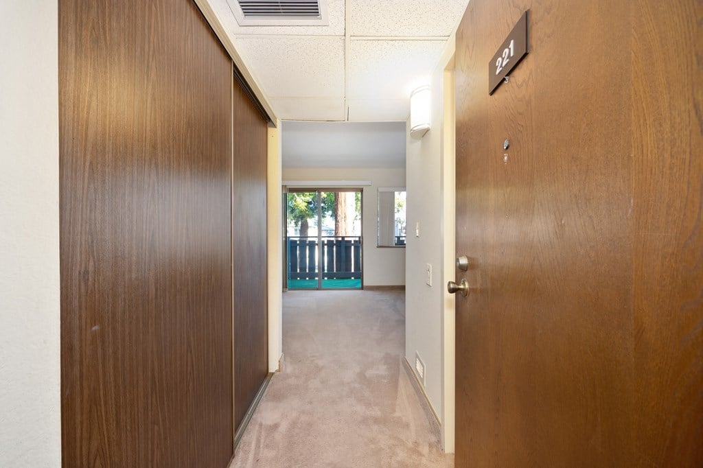 a hallway with a wooden door open to a room with a balcony