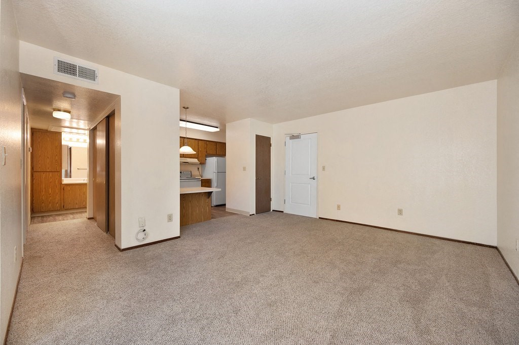 an empty living room with a kitchen in the background