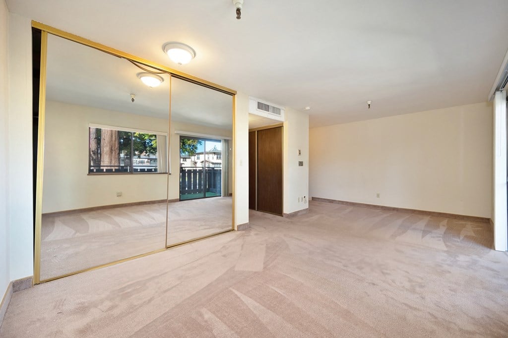 an empty living room with a large mirror and a door to a balcony