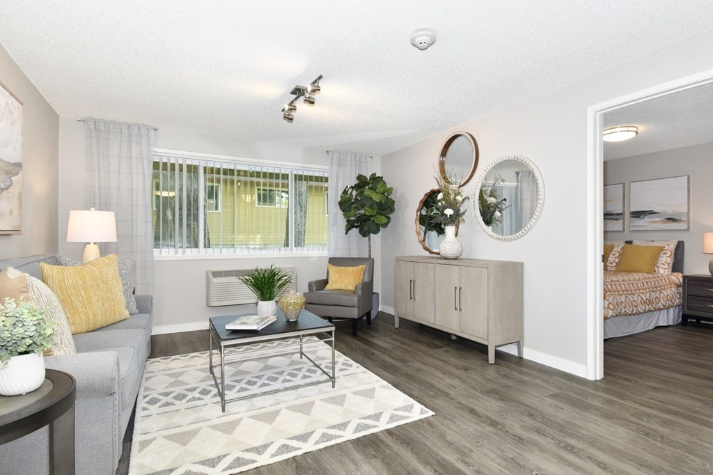 A well-lit living room with a grey couch, a coffee table, and a large mirror on the wall.