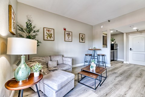 A living room with a grey couch, a wooden coffee table, and a green vase on a wooden table.