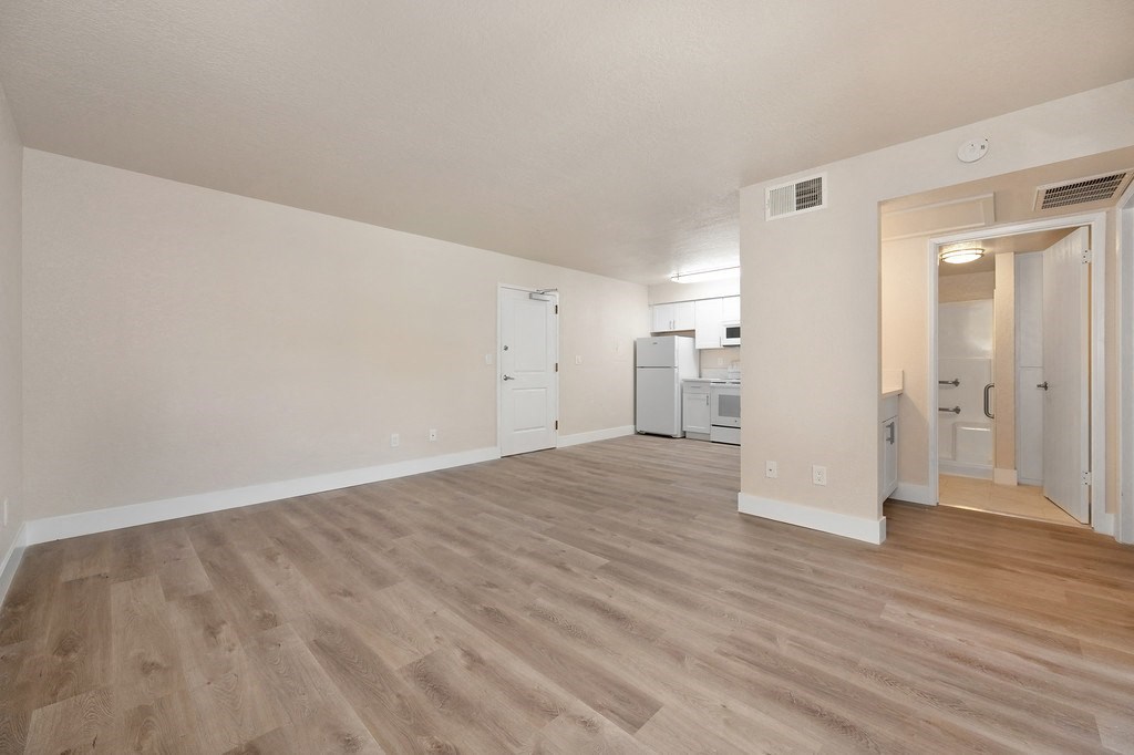 a bedroom with hardwood flooring and a kitchen in the background