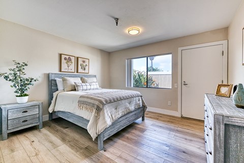 A bedroom with a bed, nightstand, and a plant.