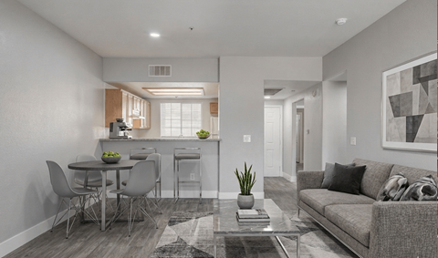 A modern living room with a grey couch, a glass coffee table, and a dining table with chairs.