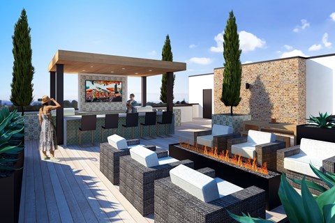 A woman in a floral dress walks on a wooden deck past a fire pit and seating area.