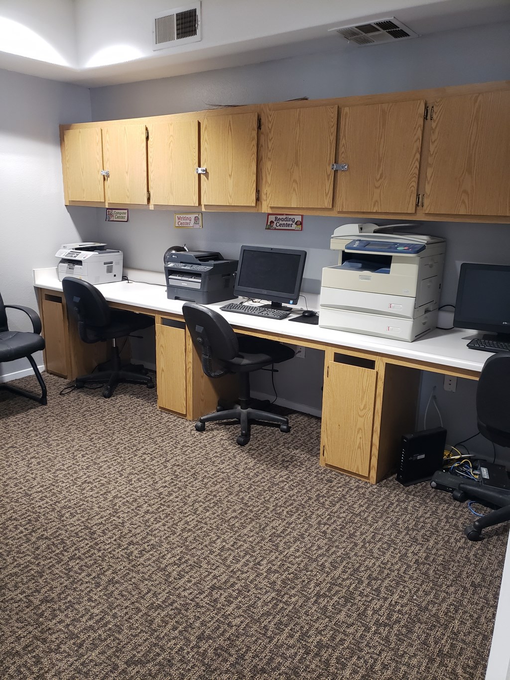 A room with a carpeted floor and a row of computers on a desk.