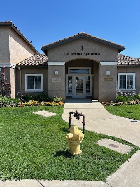 A yellow fire hydrant is in front of the entrance to Los Arboles Apartments.