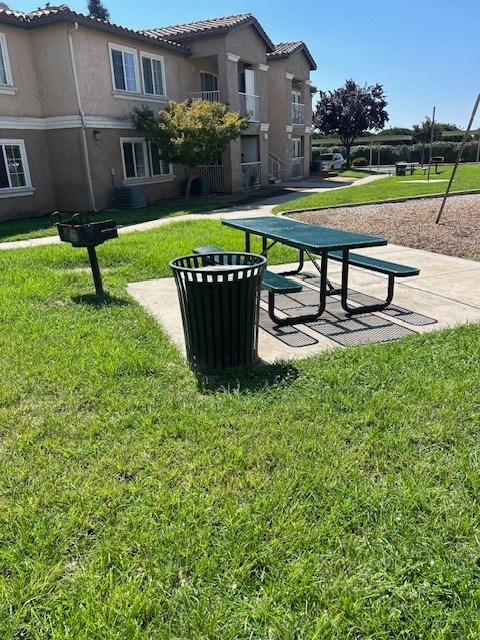 A green trash can sits next to a green picnic table.