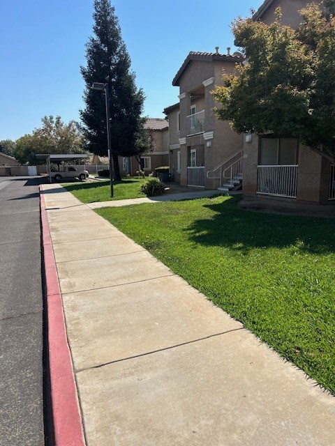 A sidewalk runs along a grassy area in front of apartment buildings.
