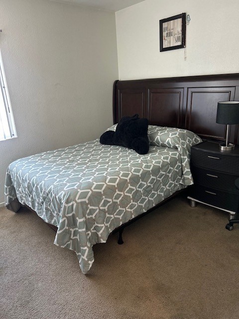 A bed with a patterned sheet and a black pillow is in a room with a wooden headboard.