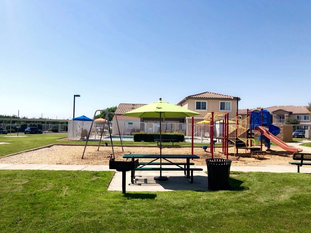 A playground with a green umbrella and a slide.