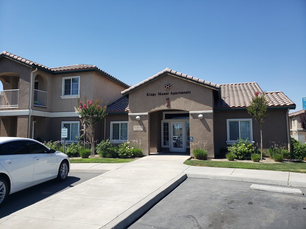 A white car is parked in front of King Maer Apartments.