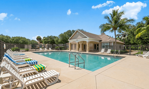 A pool with sun loungers and a house in the background.