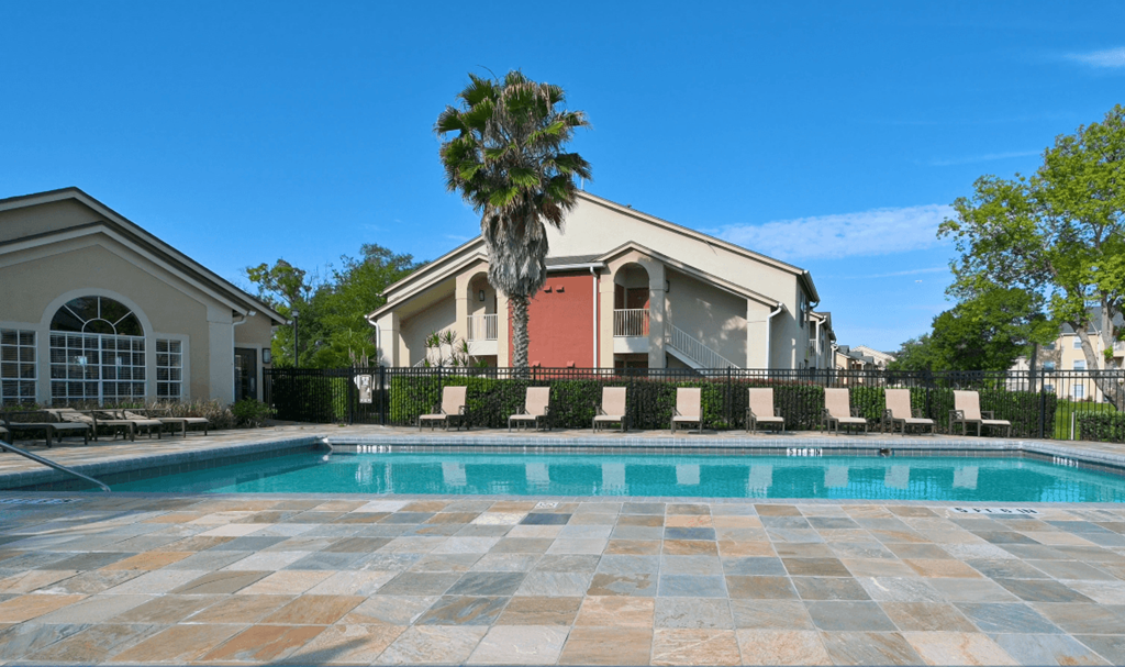 A swimming pool surrounded by a stone patio and a house with a palm tree in front.