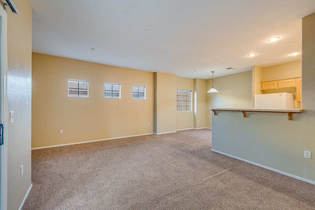 the living room and kitchen of an empty home with carpeted floors and a counter